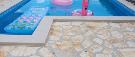 En pool med rosa flamingofigurer som flyter i vattnet, ett flytande biljardbord och stenplattor.