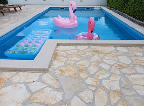 Ein Swimmingpool mit rosa Flamingo-Schwimmsachen, einem schwimmenden Pooltisch und Steinfliesen.