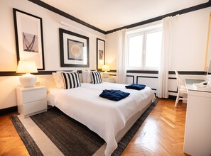 A hotel room with a large bed, two bedside tables, a desk, and a window with curtains.