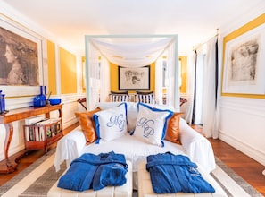 A bed with white linens and blue pillows, a wooden side table with books, a blue robe, and a framed picture on the wall. - Villa Mey's Place (Dubrovnik)