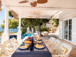 A covered outdoor dining area with a pool view, wicker furniture, and a table set for a meal.