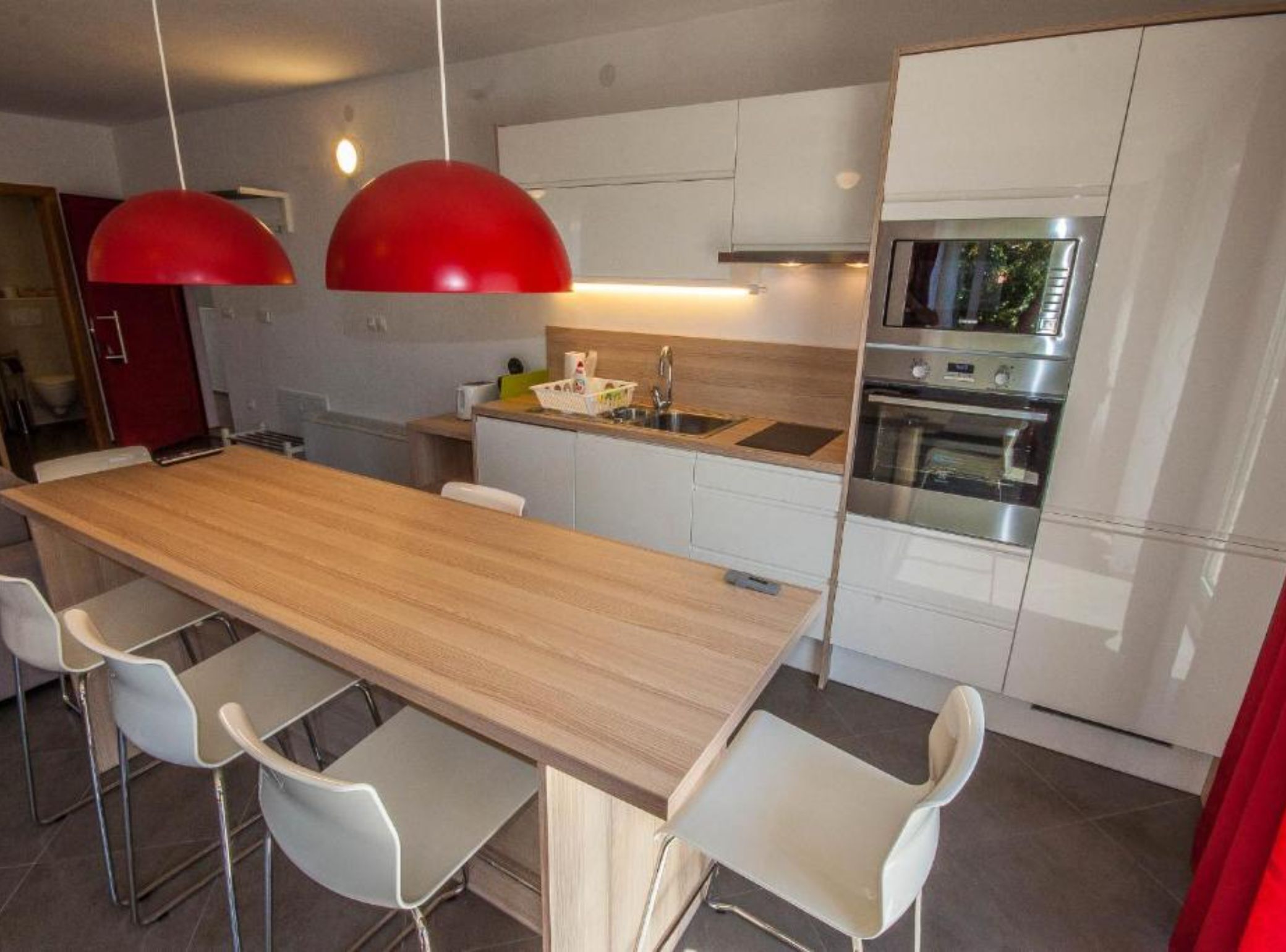 Une cuisine moderne avec un îlot central en bois, des meubles blancs et des suspensions rouges.