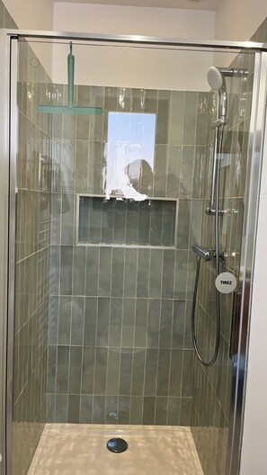Eine Duschkabine mit Handbrause, Wandarmatur und Ablaufrinne.