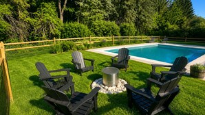 Um quintal com piscina, quatro cadeiras Adirondack, um espaço para fogueira e cerca de madeira.