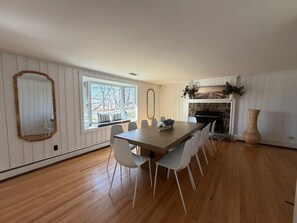 Ein Esszimmer mit einem großen Holztisch, weißen Stühlen, einem Kamin und einem großen Spiegel an der Wand.