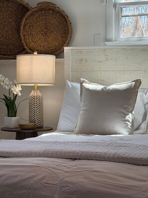 A neatly made bed with white bedding, a bedside lamp, a potted plant, and a textured wall. - Litchfield Hills Modern Design Escape w/ a Pool (Sharon)