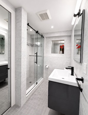 A modern bathroom with a glass-enclosed shower, a vanity with a black sink, and a mirror with a red flower vase. - Litchfield Hills Modern Design Escape w/ a Pool (Sharon)