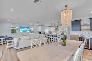Eine moderne Küche mit weißen Schränken, eine Essecke mit Holztisch und ein Wohnzimmer mit weißem Sofa und blauen Stühlen.