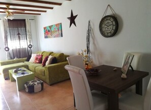 Ein Wohnzimmer mit einem grünen Sofa, einem Esstisch, einem weißen Stuhl, einer Uhr und einer Stern-Dekoration an der Wand.