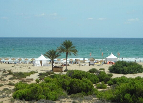 Ein Strand mit Zelten, Sonnenschirmen und Palmen.