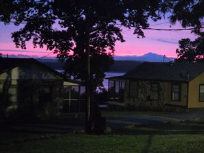 A house with a large tree in front, a small porch, and a view of a body of water and mountains in the background. - LAKE NORFORK cottages at a FANTASTIC FISHING resort,1-2bedrooms,electric trolley (Gamaliel)