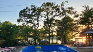 Piscina com vista clara para árvores e um gazebo ao fundo.