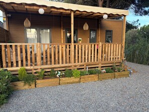 A wooden cabin with a covered porch, outdoor seating, and a gravel driveway. - Cosy 3 bed mobile home, swimming pool (La Crau)