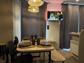 Een eethoek met een televisie, rieten stoelen en een tafel gedekt voor vier personen.