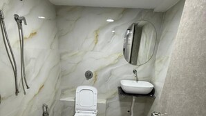 Un baño con inodoro, lavabo, espejo, ducha y un cubo rojo.
