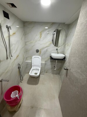Ein Badezimmer mit Toilette, Waschbecken, Spiegel, Dusche und einem roten Eimer.