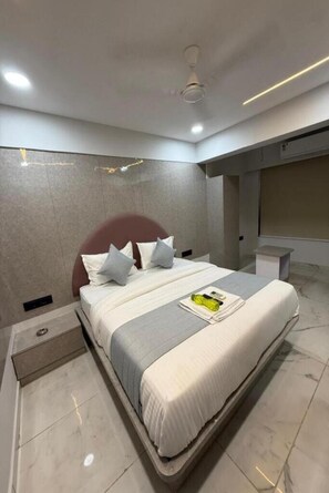 Ein modernes Hotelzimmer mit einem großen Bett, einem Deckenventilator, eingelassener Beleuchtung und einem Marmorboden.
