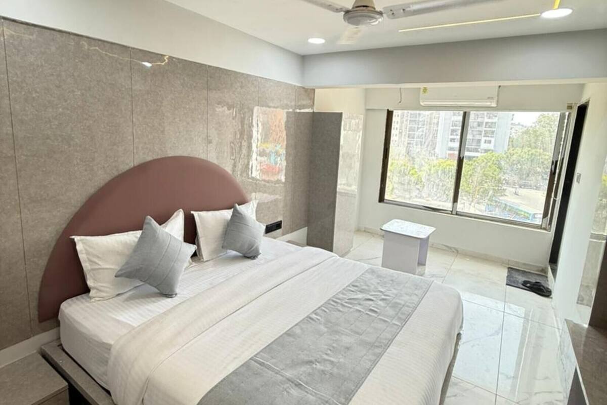 A modern bedroom with a large bed, a ceiling fan, and a window with a city view.