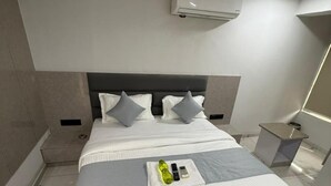 Una habitación de hotel moderna con una cama grande, un cabecero, un equipo de aire acondicionado, una mesita de noche y una pequeña mesa auxiliar.