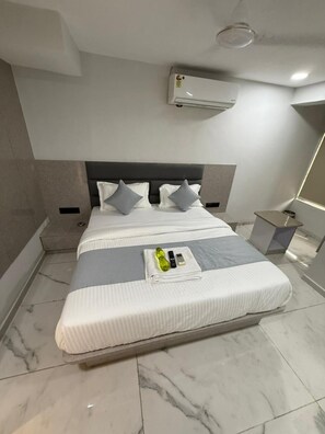 Ein modernes Hotelzimmer mit einem großen Bett, einem Kopfteil, einer Klimaanlage, einem Nachttisch und einem Beistelltisch.