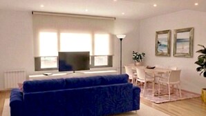 Ett modernt vardagsrum med en soffa, TV, matbord, stolar och ett stort fönster.