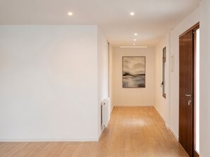Ein Flur mit Holzboden, weißen Wänden, eingelassenen Deckenleuchten und einer Tür rechts.