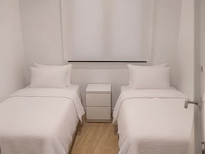 Ein kleines, sauberes Zimmer mit zwei Einzelbetten, einem Nachttisch und einem an der Wand befestigten Regal.