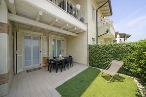 A covered patio with a table and chairs, a small garden area with artificial grass, and a hedge. - Francy House: Pool, Relaxation, Lake Garda, A/C, WiFi (Castelnuovo del Garda)