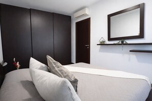 A bedroom with a bed, dark wardrobe, white walls, and a mounted mirror. - Francy House: Pool, Relaxation, Lake Garda, A/C, WiFi (Castelnuovo del Garda)