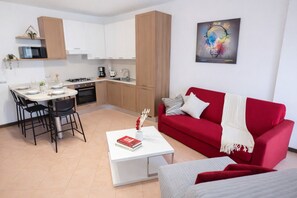 A modern apartment with a dining area, kitchen, red sofa, and a painting on the wall. - Francy House: Pool, Relaxation, Lake Garda, A/C, WiFi (Castelnuovo del Garda)