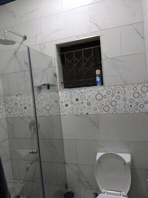 Et badeværelse med en glasafskærmet brusekabine, toilet og mønstrede fliser.