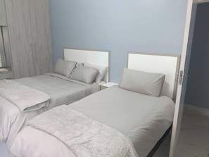 A hotel room with two beds, a wardrobe, and a door. - Crompton Apartments 786 (Durban)