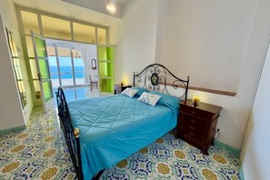 A bedroom with a bed, a nightstand, a dresser, and a view of the sea through a glass door. - Caravella Nina Praiano  (PRAIANO)