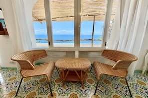 Een kamer met uitzicht op zee, een rieten tafel en twee stoelen.