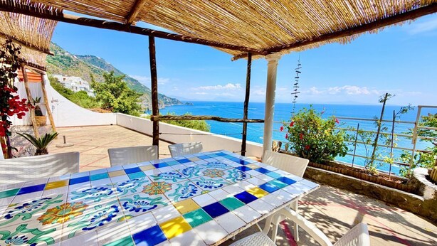 Un espacio al aire libre techado con una mesa y sillas de cerámica, con vistas a la costa.
