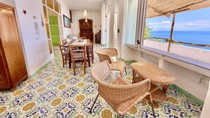 Una habitación con una mesa de comedor, sillas, un sofá de mimbre, suelo estampado y vistas al mar.