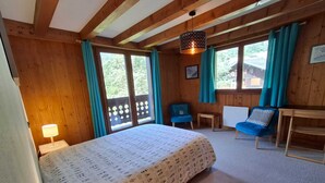 A wooden room with a bed, a desk, a chair, and a window with curtains. - Our family chalet in the heart of the Alps (Chamonix-Mont-Blanc)