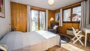 A room with a bed, a desk, a chair, and large windows with curtains. - Our family chalet in the heart of the Alps (Chamonix-Mont-Blanc)