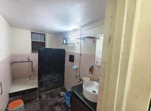 A bathroom with a toilet, sink, mirror, shower, and a blue bucket.