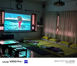 A living room with a large flat-screen TV, a sofa, a small table, and a projector.