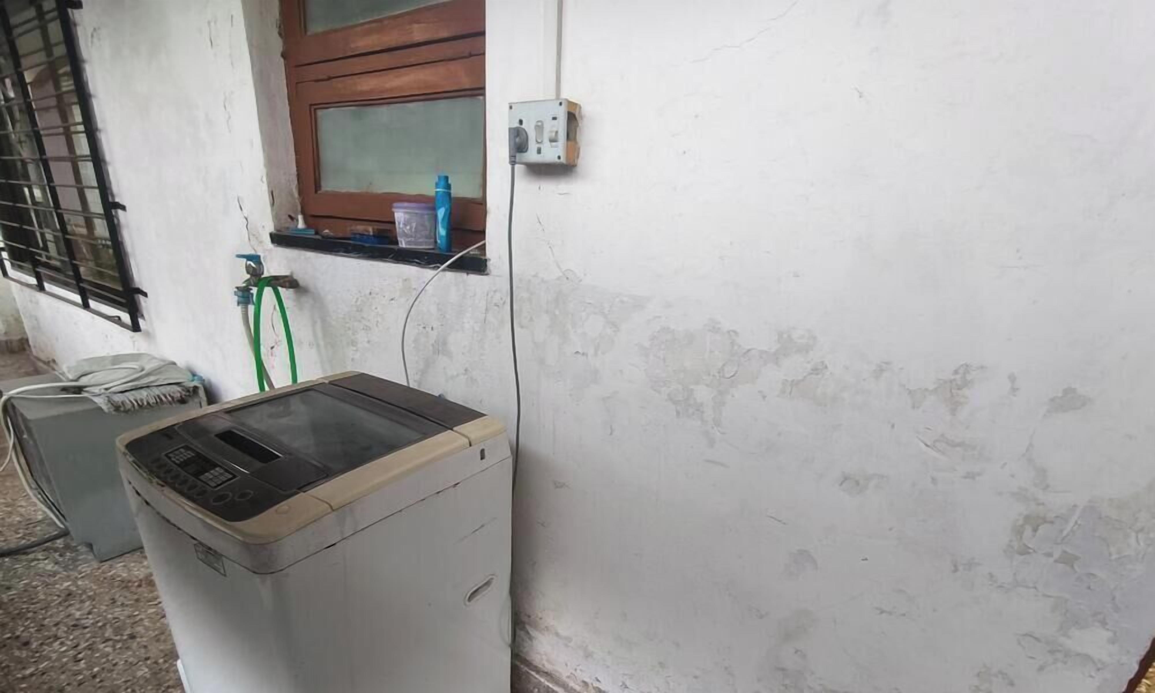 A washing machine, a window with a wooden frame, and a power outlet on a white wall.