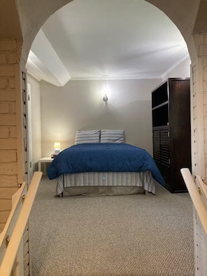 Quarto com cama, mesa de cabeceira, abajur e guarda-roupa.