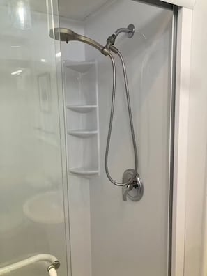 Um chuveiro com box de vidro, com chuveiro manual e mangueira flexível.