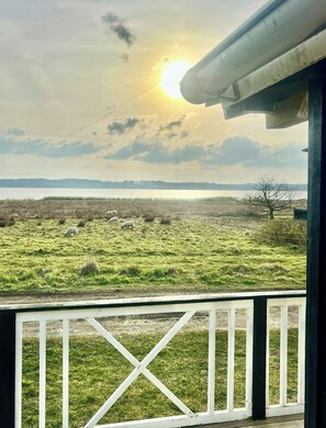 Une vue depuis un balcon donnant sur un champ verdoyant, avec un plan d’eau et des collines au loin.