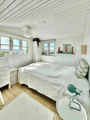 A bedroom with a bed, dresser, bedside table, lamp, and a window with a view.