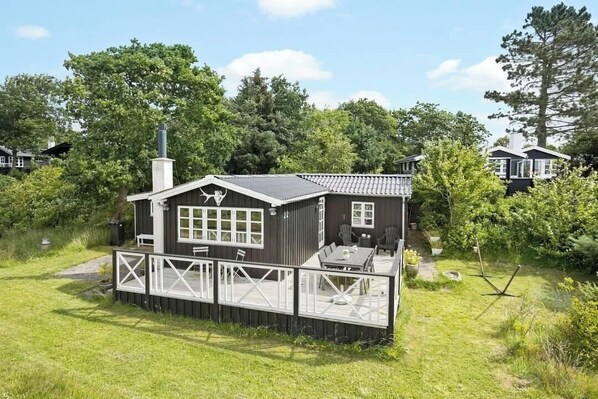 A small cabin with a deck, surrounded by greenery.