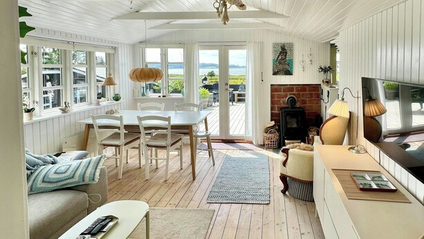 A cozy living room with a dining area, a fireplace, and large windows offering a view. - Two houses with a view of the fjord (Nibe)