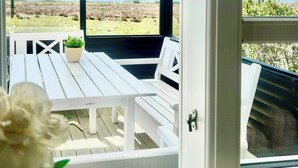 A covered outdoor seating area with white furniture, a potted plant, and a view of a lake and distant hills. - Two houses with a view of the fjord (Nibe)