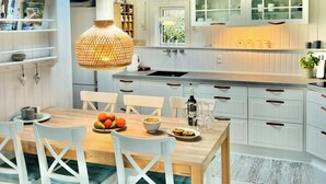 A modern kitchen with white cabinetry, a dining table with chairs, a hanging light fixture, and a window providing natural light. - Two houses with a view of the fjord (Nibe)