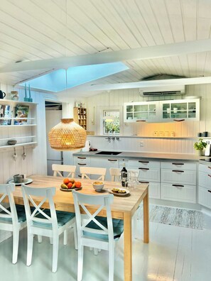 A modern kitchen with white cabinetry, a dining table with chairs, a hanging light fixture, and a window providing natural light. - Two houses with a view of the fjord (Nibe)